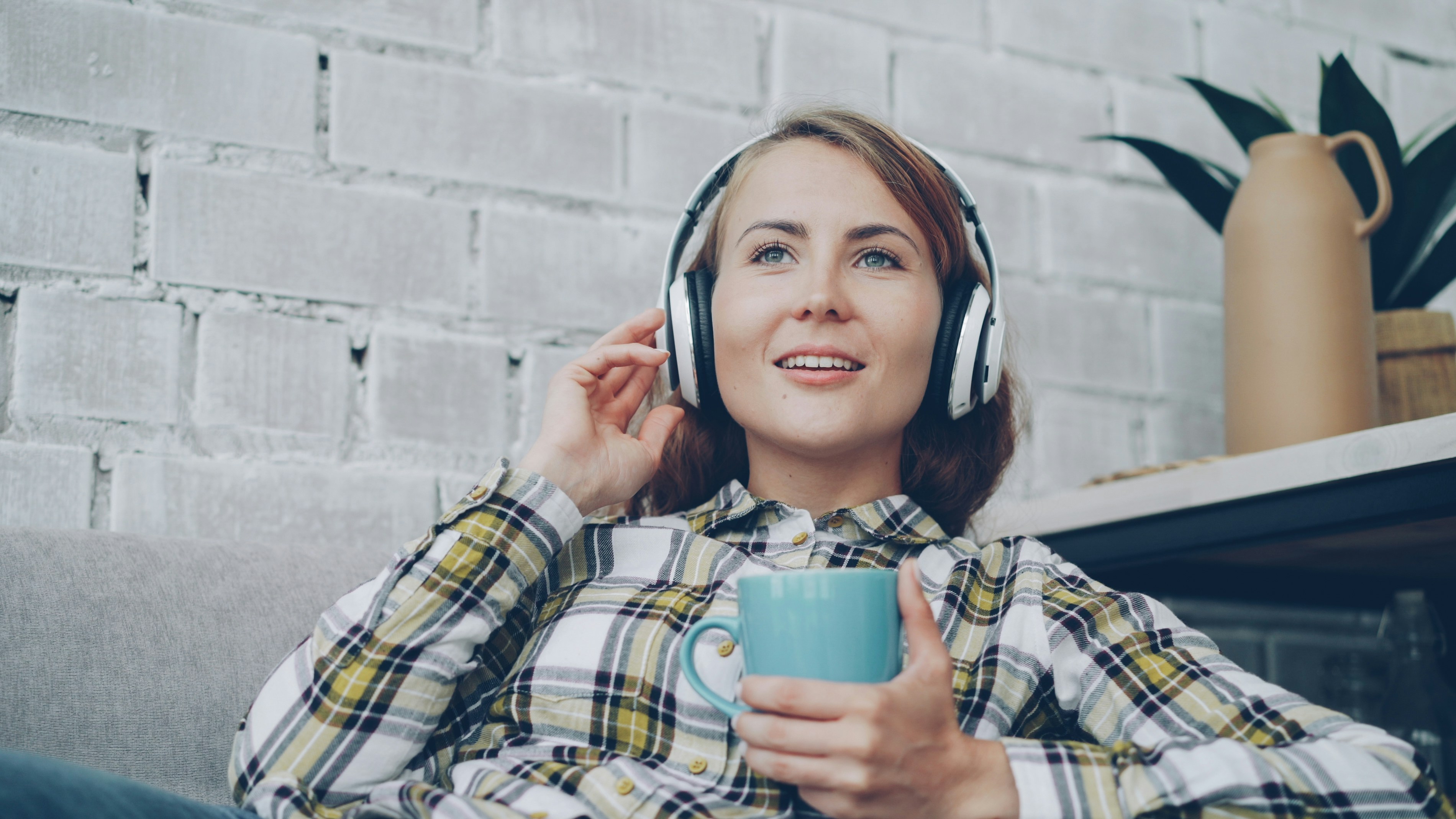 Woman wearing headphones holds a mug while listening to music.
