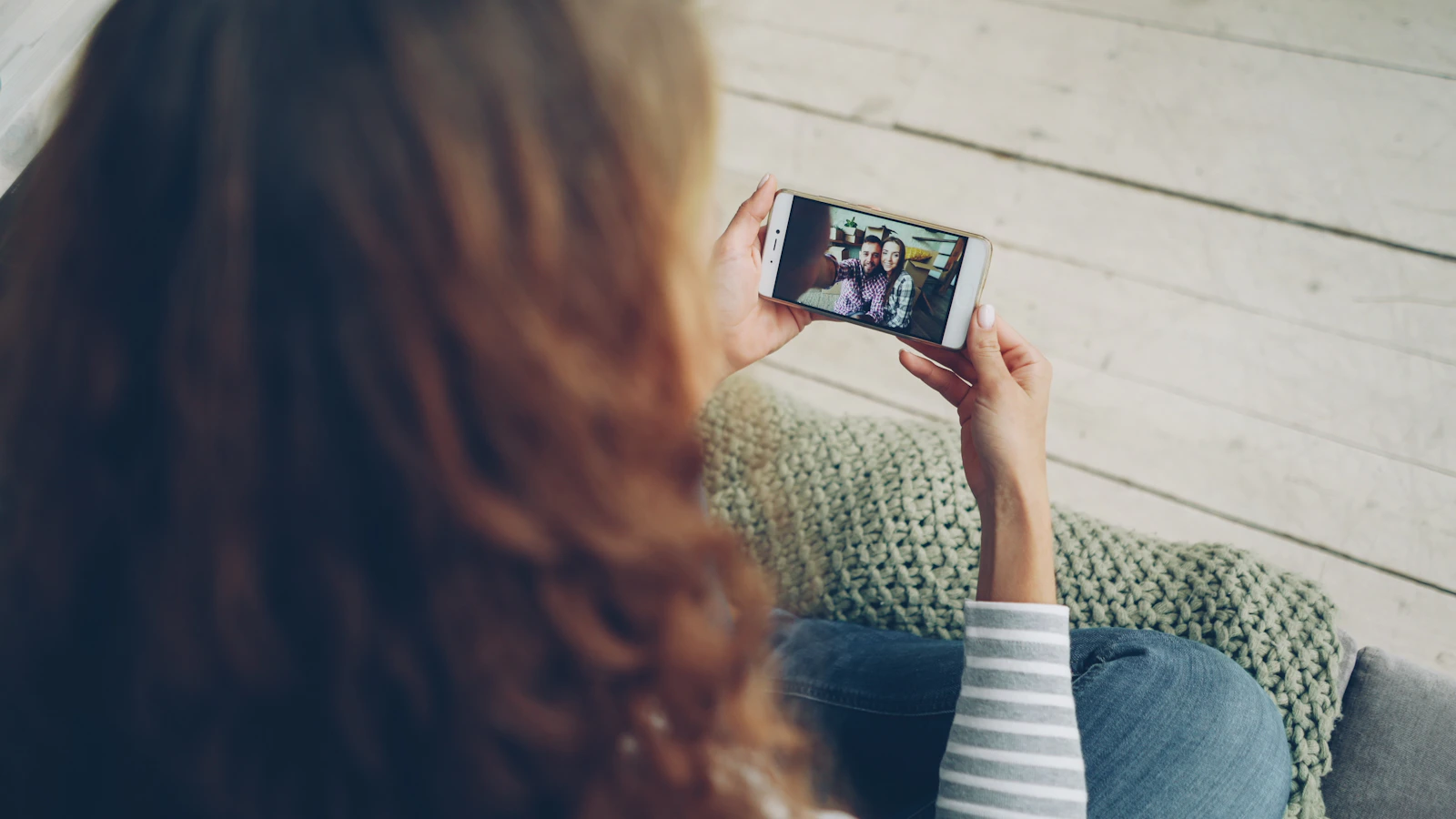 A person holding up a phone, viewed from over their shoulder, in soft natural light