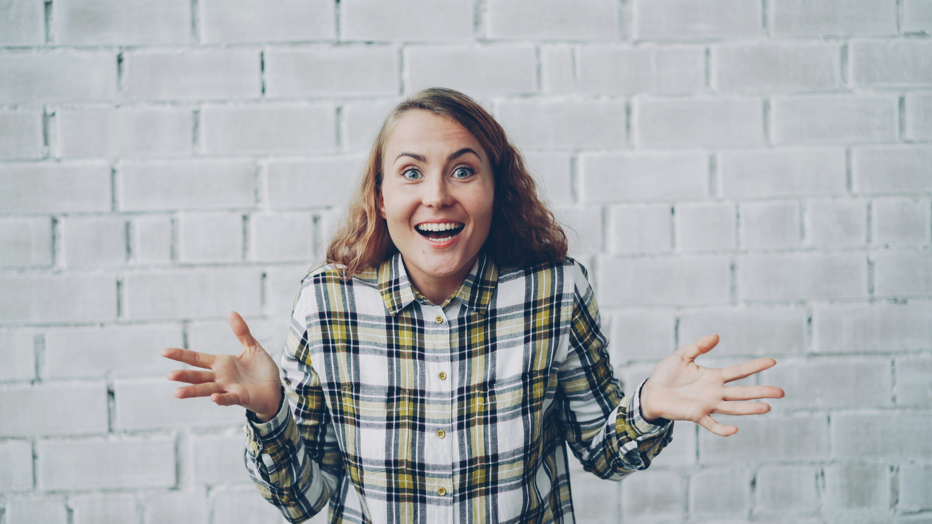 Excited woman with arms outstretched in front of brick wall