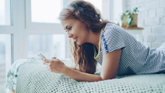 Young woman lying on bed looking at phone