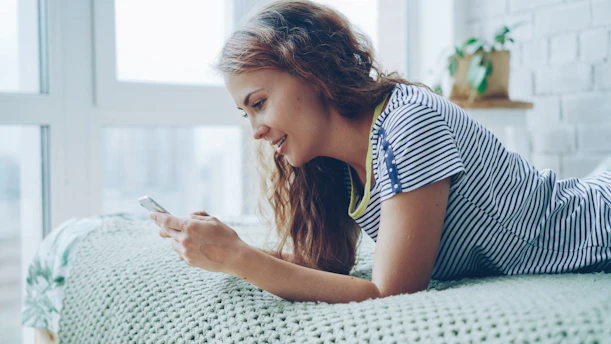 Young woman lying on bed looking at phone