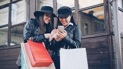 Two women looking at a smartphone with shopping bags.