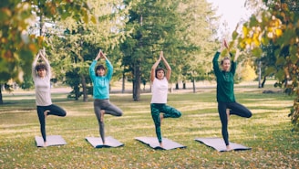 Four women practice yoga tree pose outdoors.