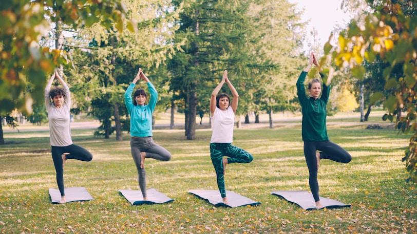 Four women practice yoga tree pose outdoors.