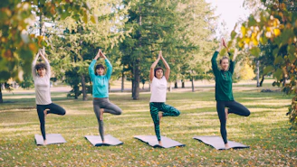 Four women practice yoga tree pose outdoors.