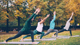 Four people practicing yoga outdoors in autumn park.