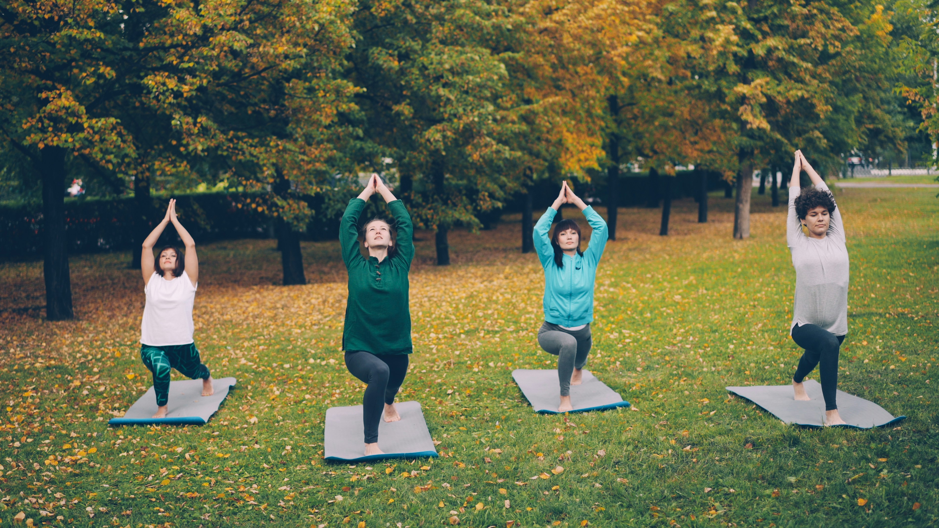 four women doing yoga in a park during fall