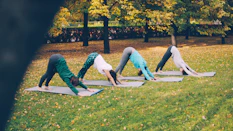 Four women practice downward-facing dog yoga pose outdoors
