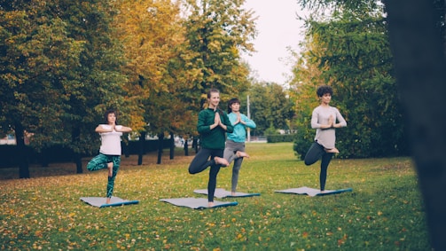 Four people doing yoga tree pose in park