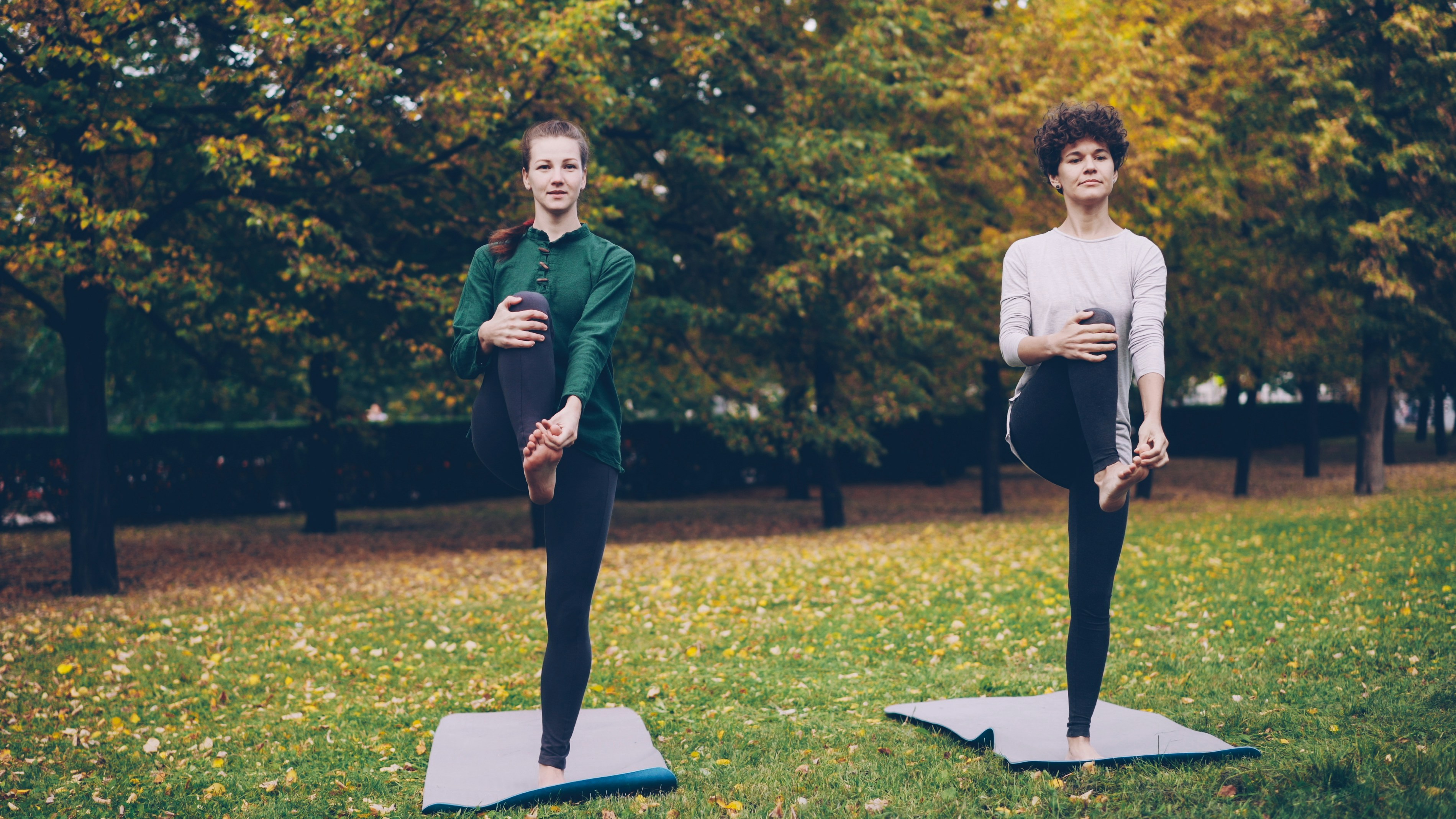 Two women doing yoga in autumn park