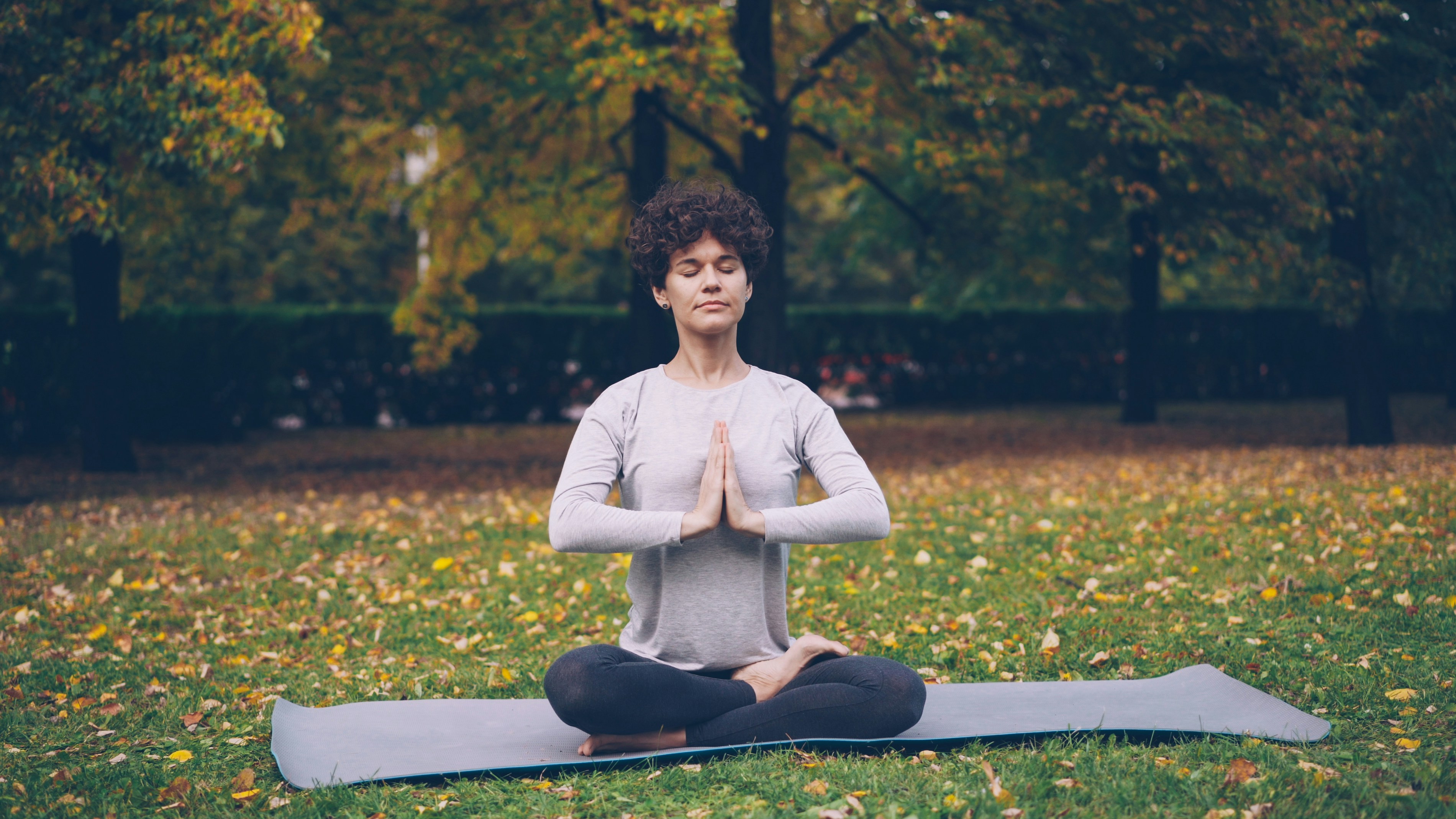 Woman meditating in lotus pose on yoga mat outdoors.