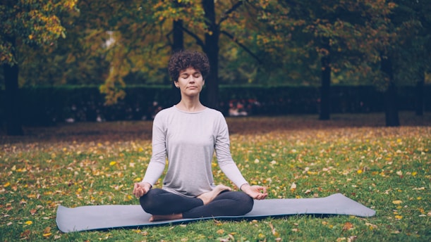Woman meditating peacefully on a yoga mat outdoors.