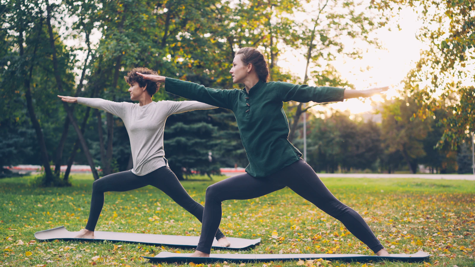 Two practitioners holding warrior pose outdoors on a bright morning