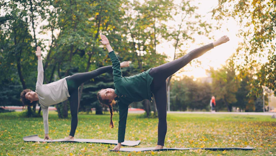 Two women practicing yoga outdoors in a park.