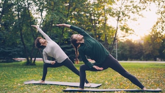 Two women practicing yoga outdoors in a park.
