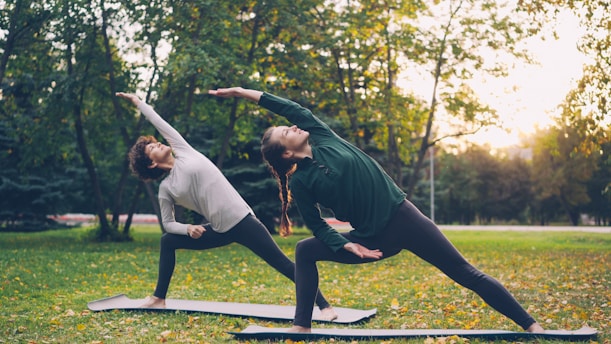 Two women practicing yoga outdoors in a park.
