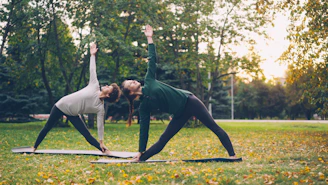 Two women practicing yoga in a park.