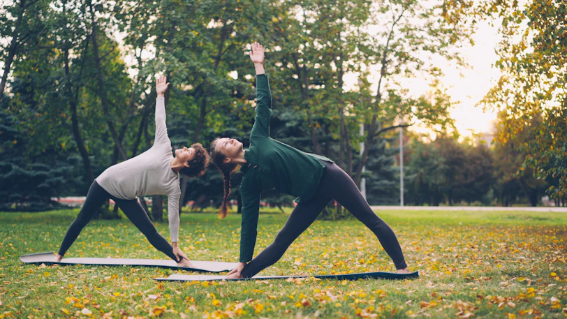Two women practicing yoga in a park.