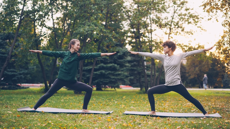 Two people practicing yoga outdoors in a park
