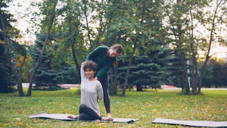 Instructor assisting woman with yoga pose in park