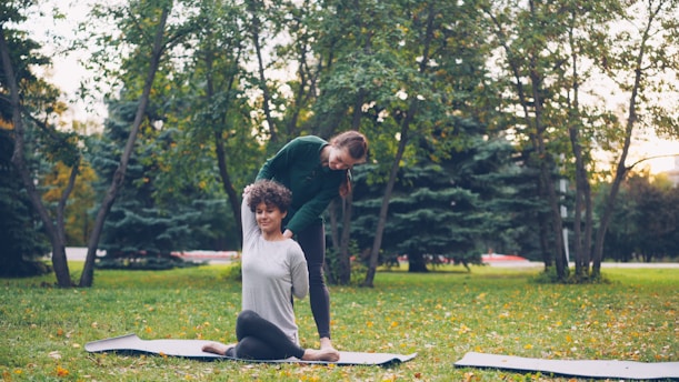 Instructor assisting woman with yoga pose in park