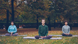 Three people meditating in a park during autumn.