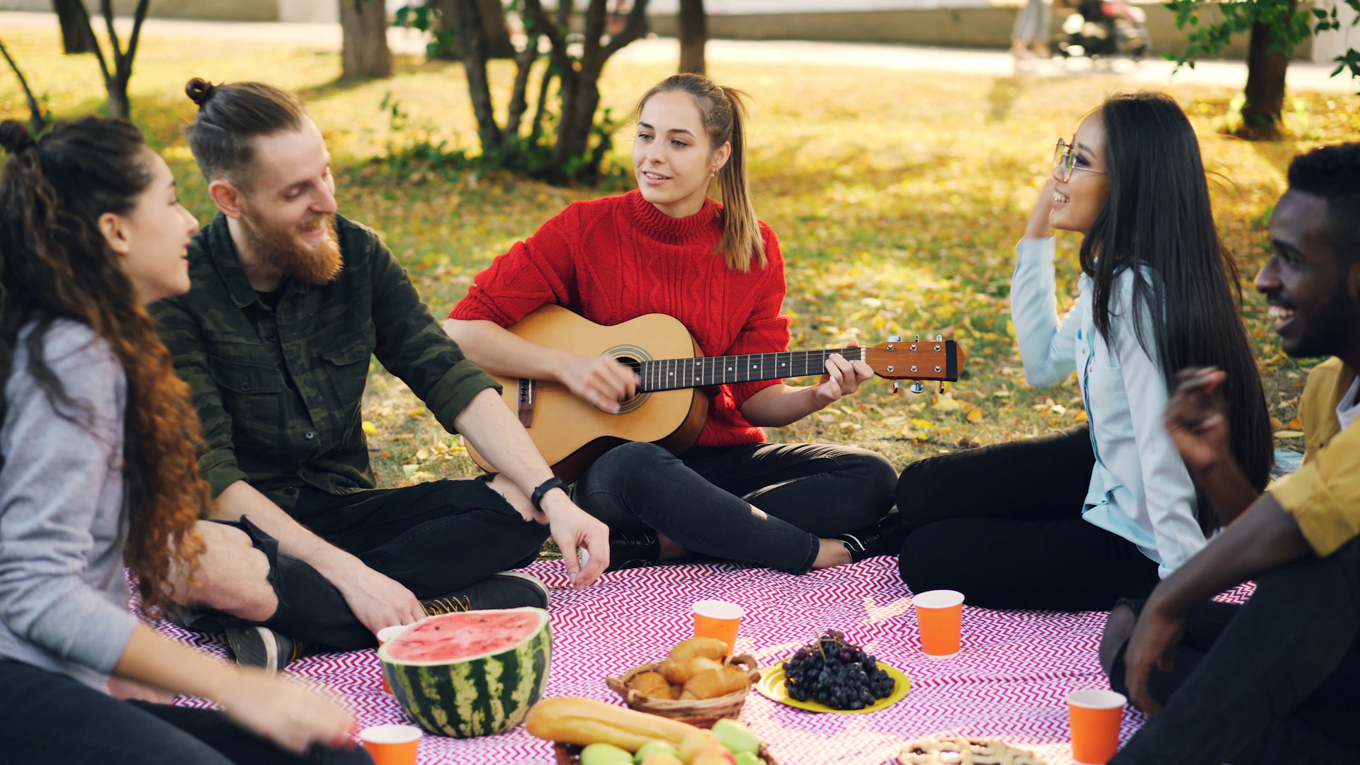 Friends enjoying a picnic and playing guitar outdoors.