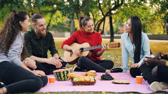 Friends enjoying a picnic and playing guitar in park.