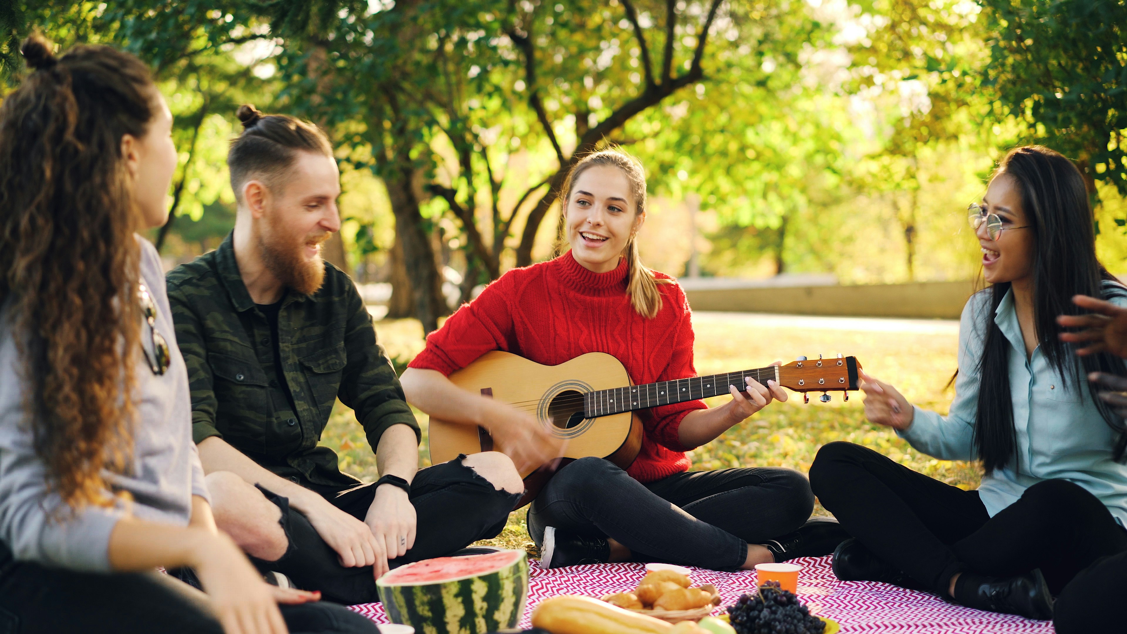 Friends enjoying a picnic and playing guitar outdoors.