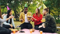 Friends celebrating birthday with cake at outdoor picnic.