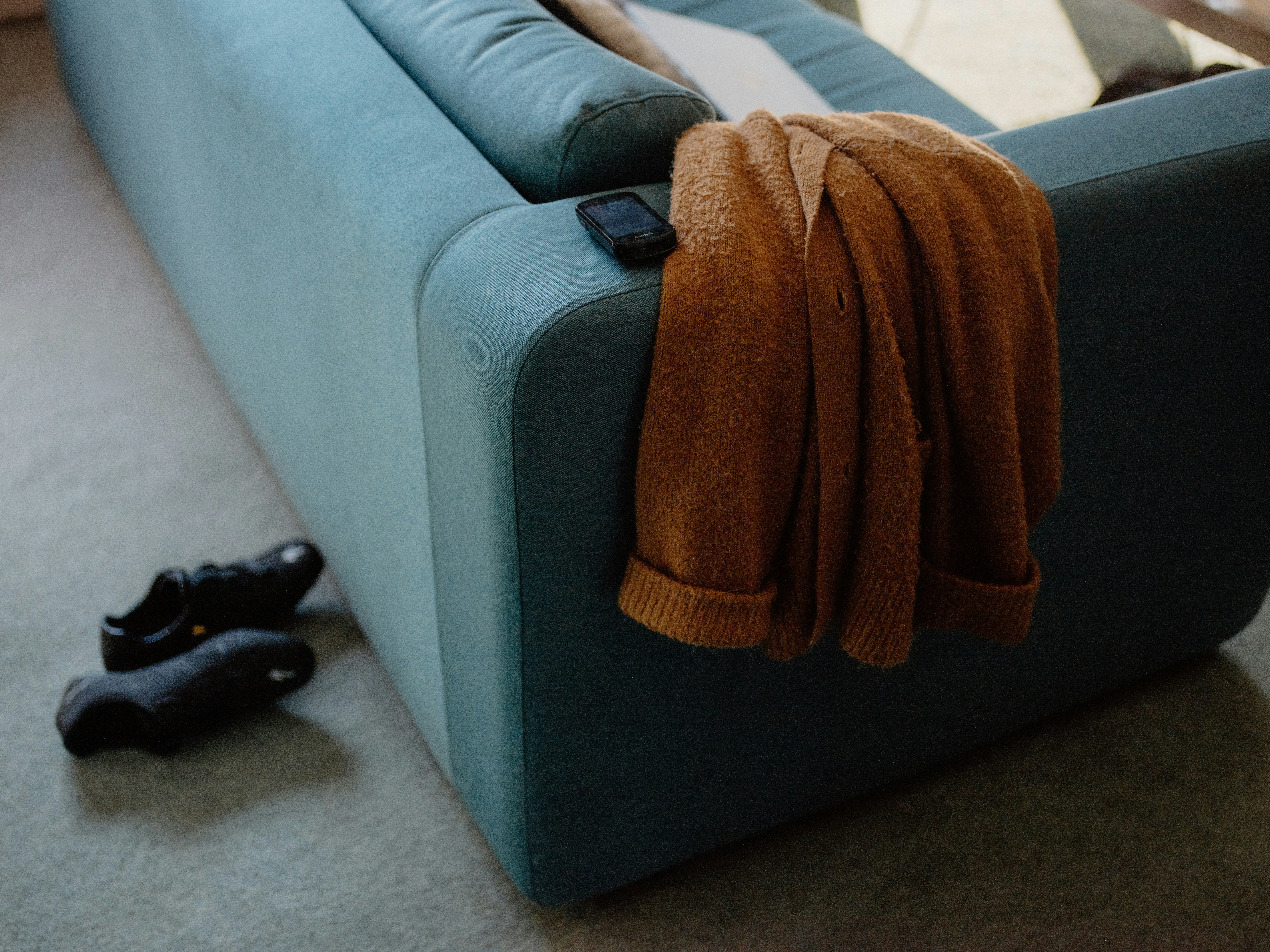 A teal couch with a sweater and shoes nearby.