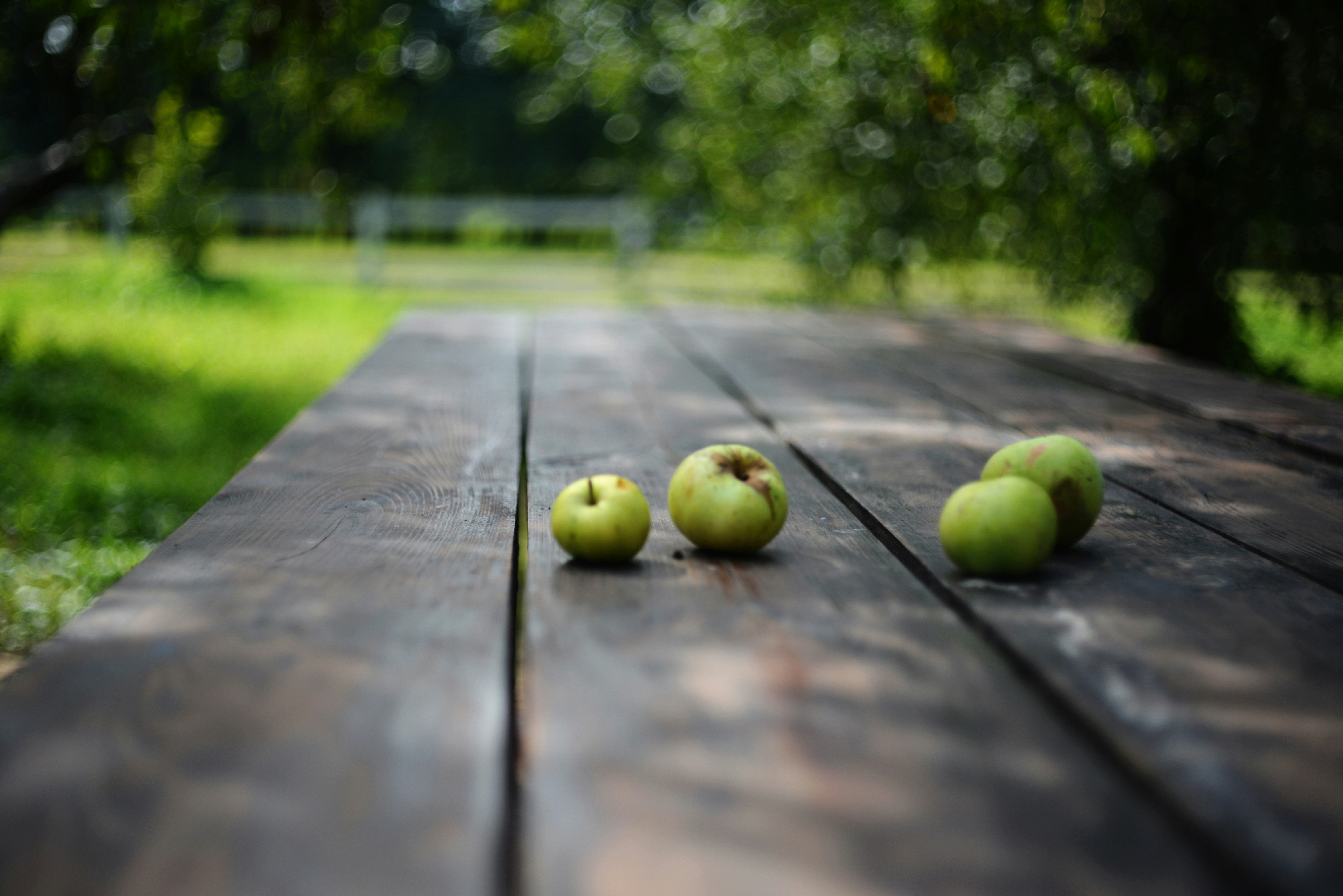 Green apples sit on a rustic wooden picnic table.