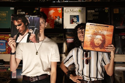 Two men hold up album covers in a record store.
