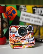 Instant camera covered in colorful stickers with skateboard.