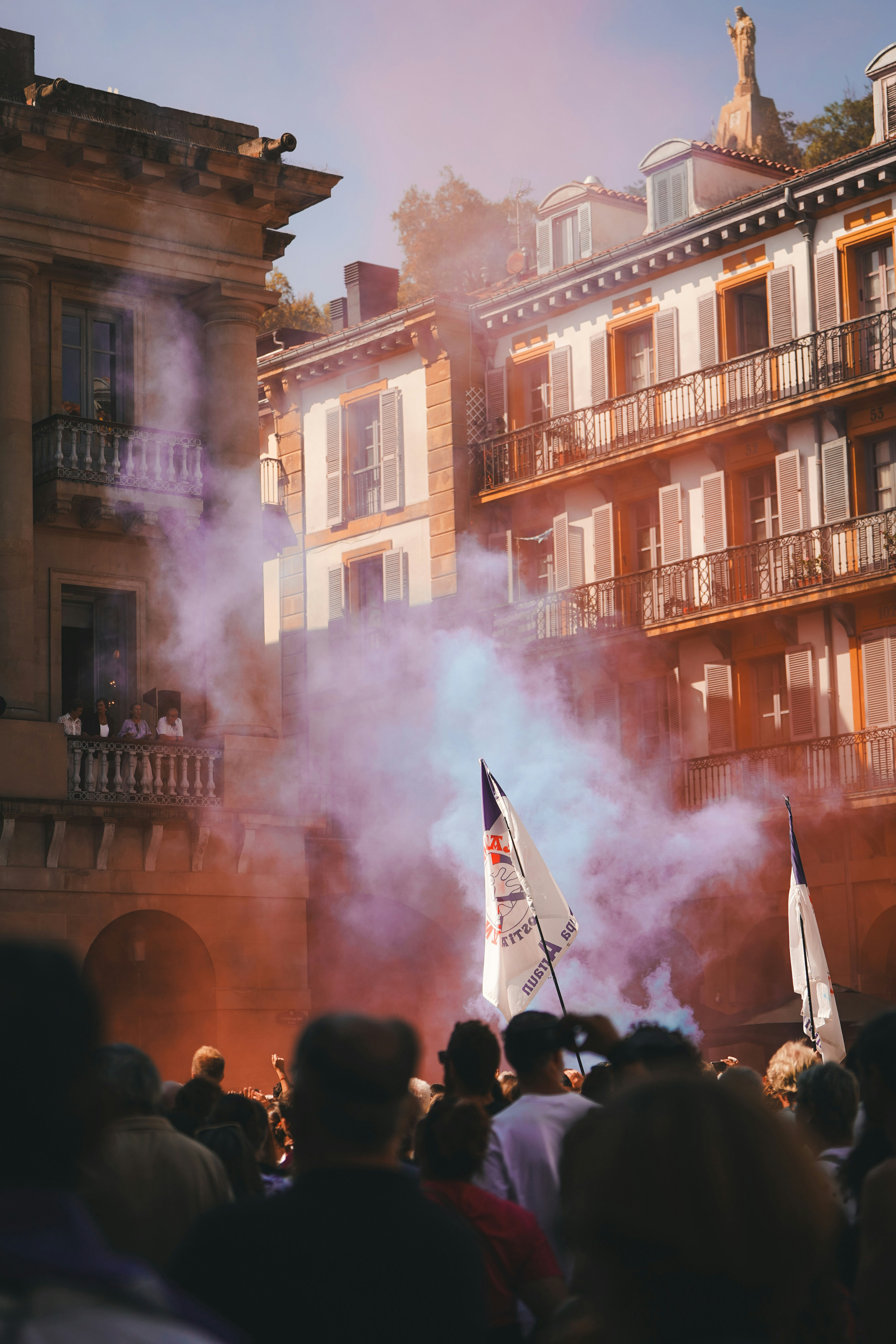 Crowd watches colorful smoke rise in city square