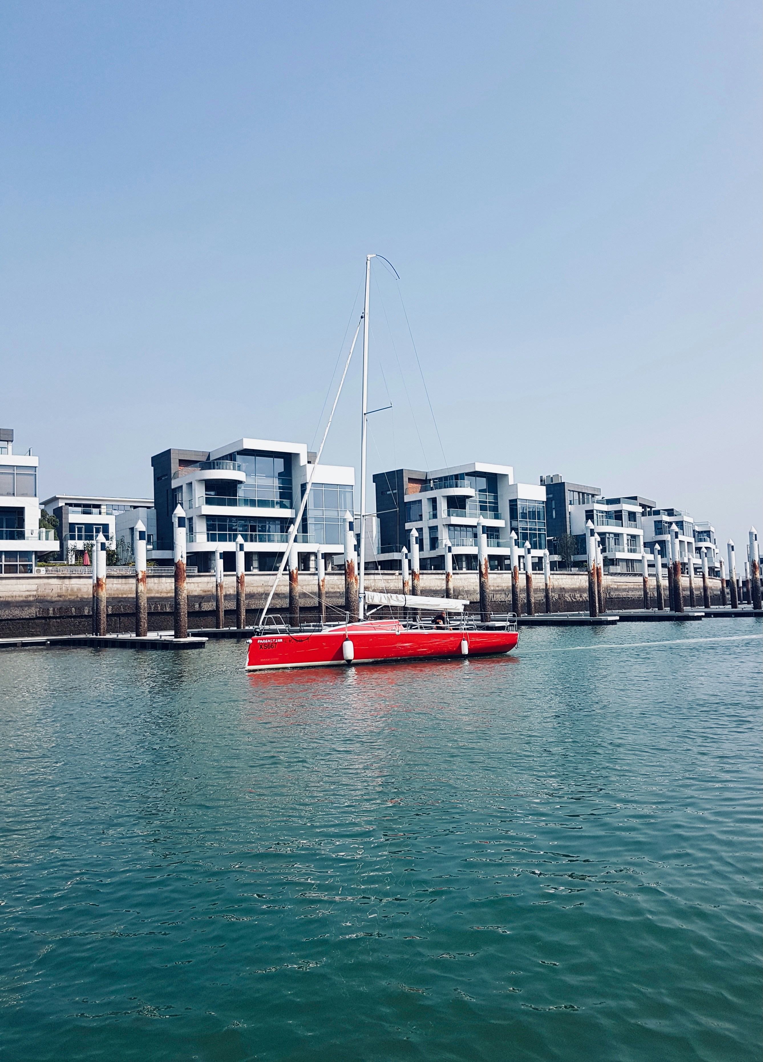 Red sailboat docked near modern waterfront buildings