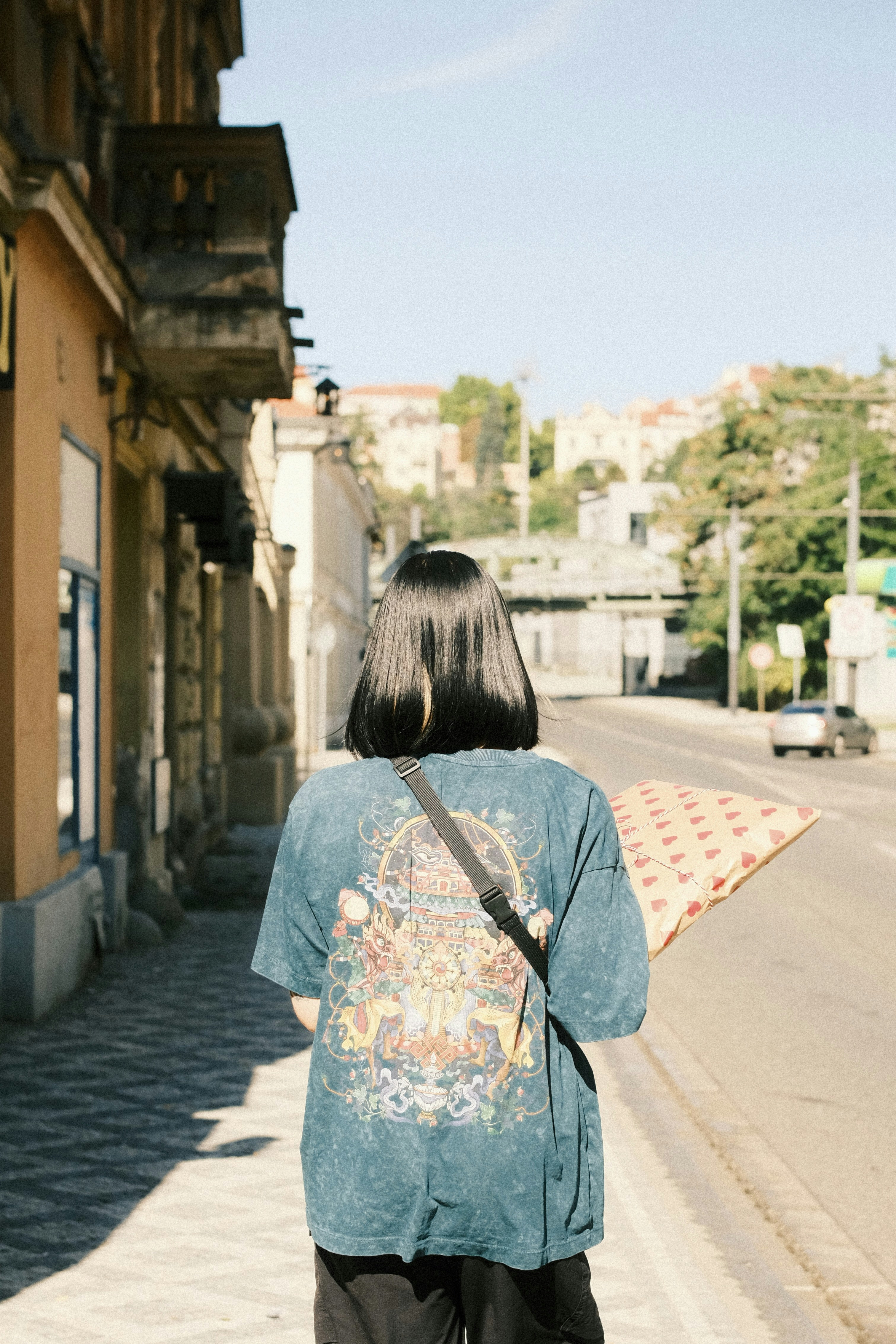 Woman walks down a sunny street carrying a pillow.