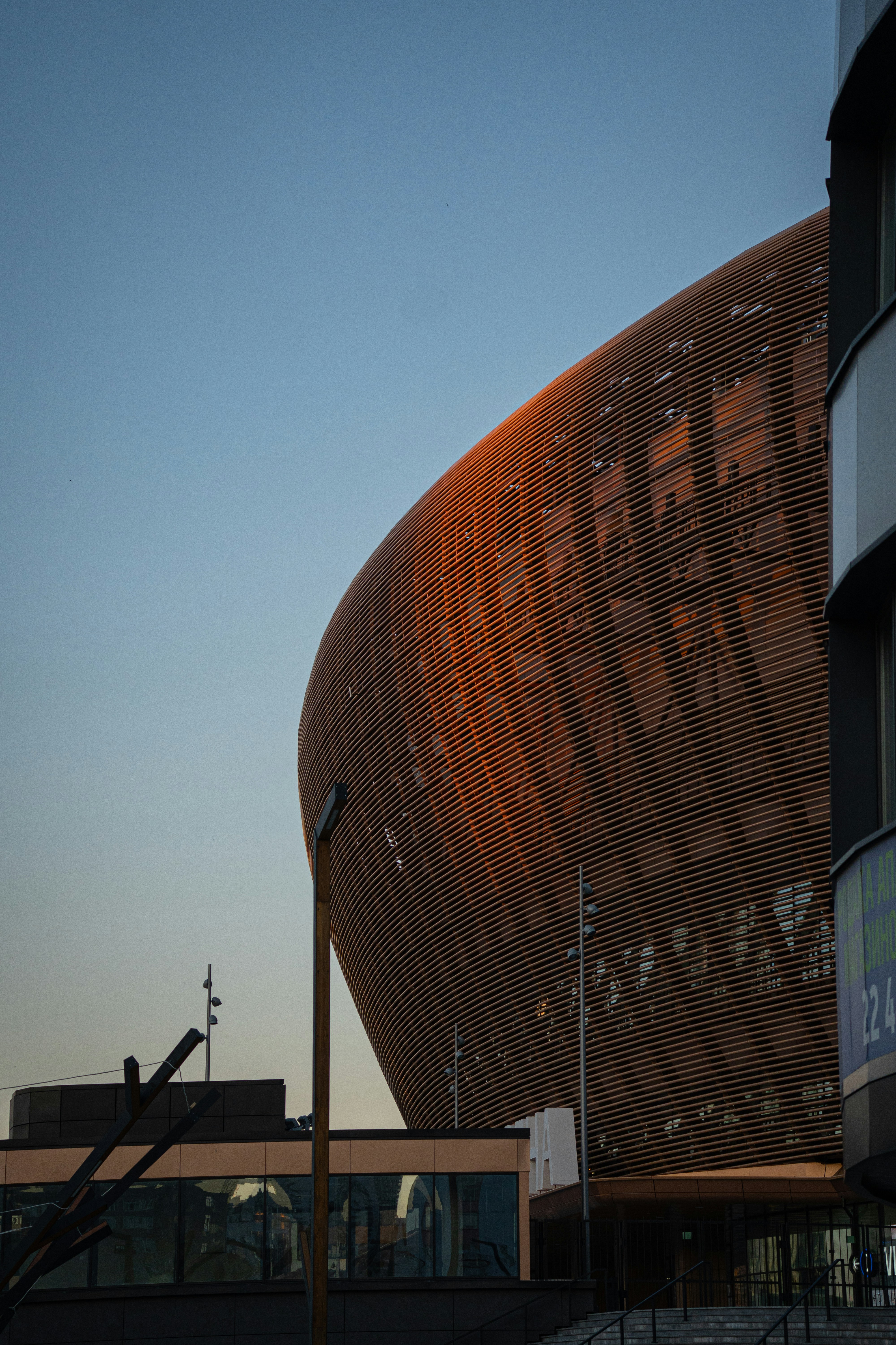 Edificio moderno con fachada curva de madera al atardecer.