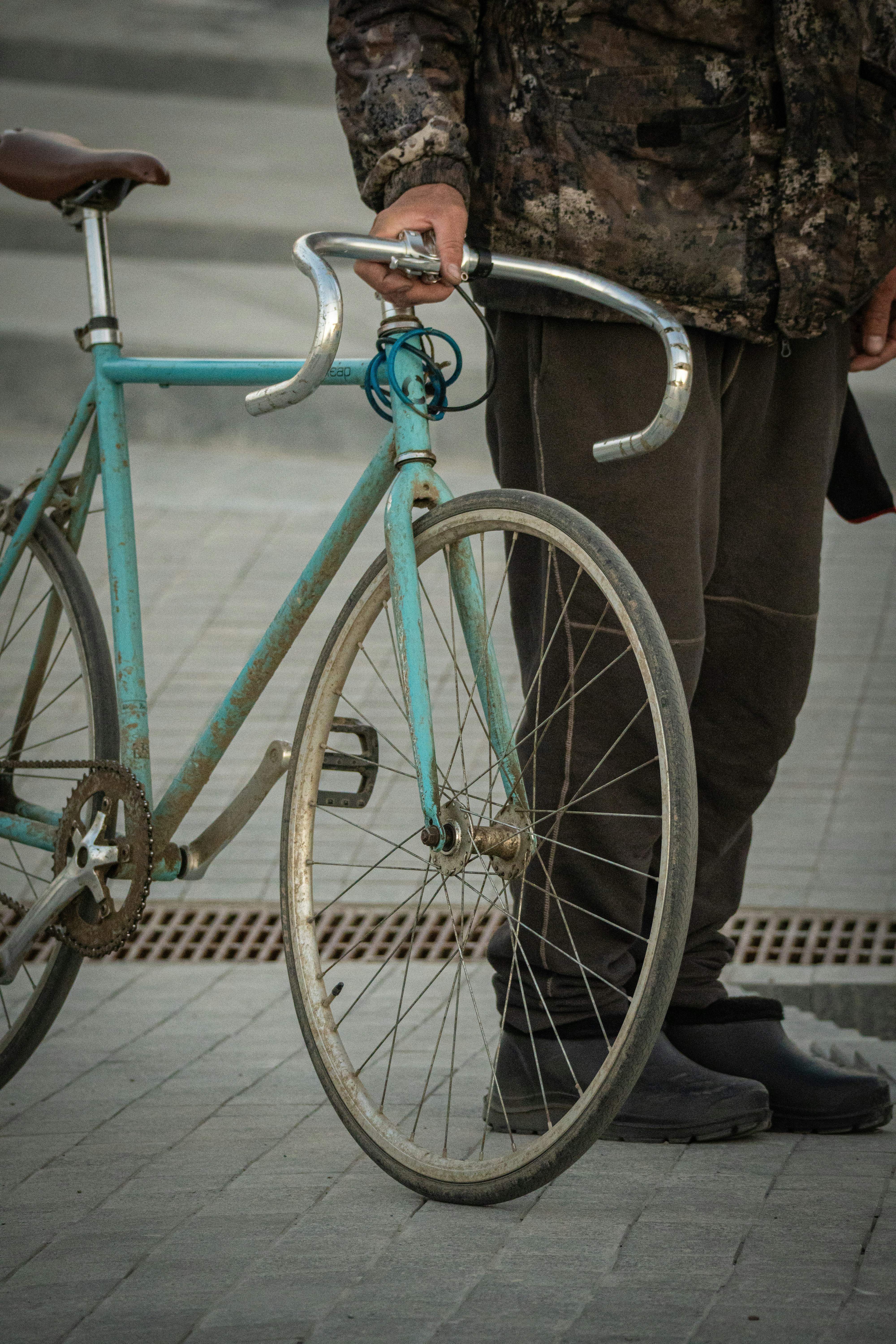 Person holding a vintage turquoise bicycle outdoors