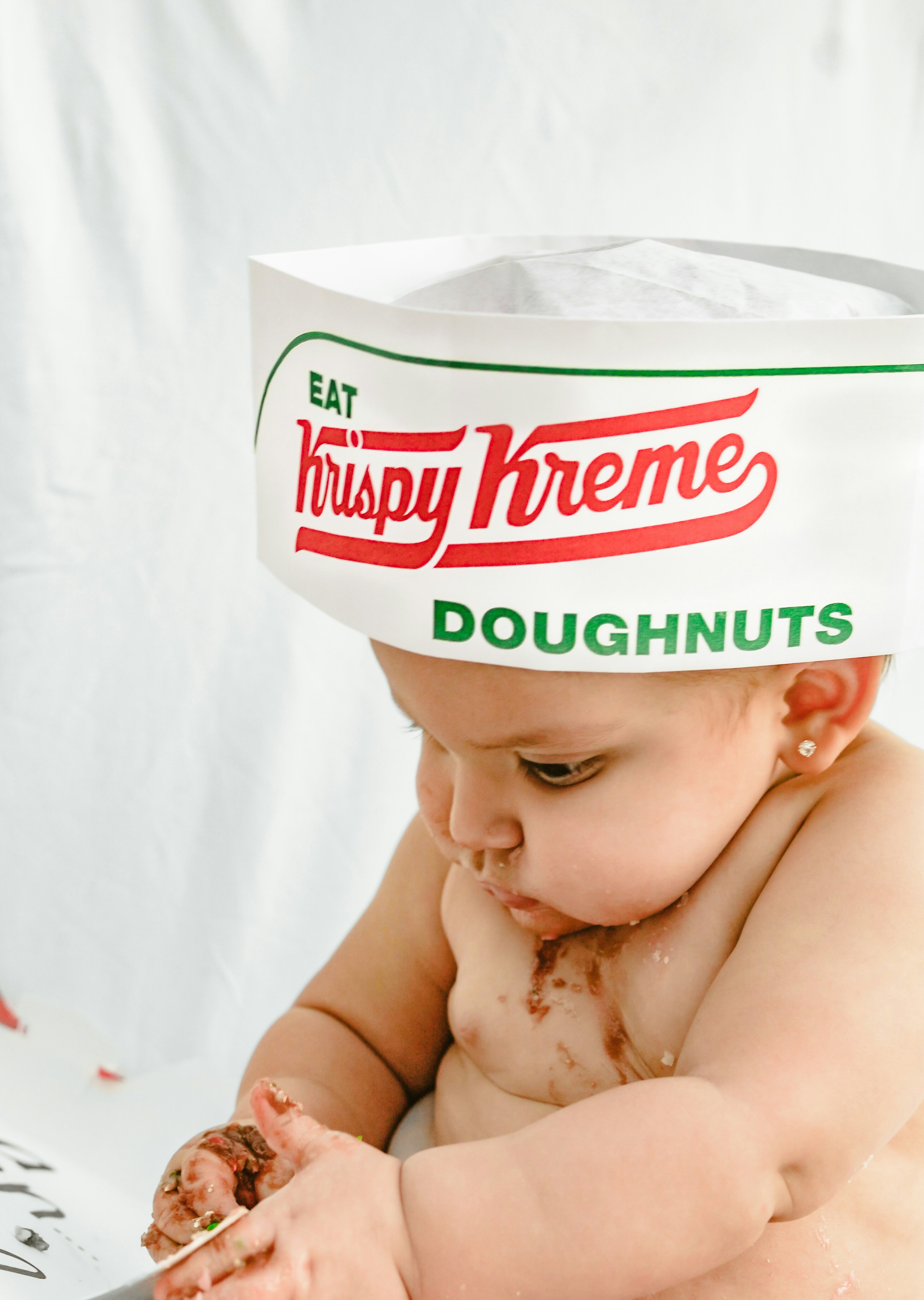 Baby wearing a krispy kreme hat messy with chocolate