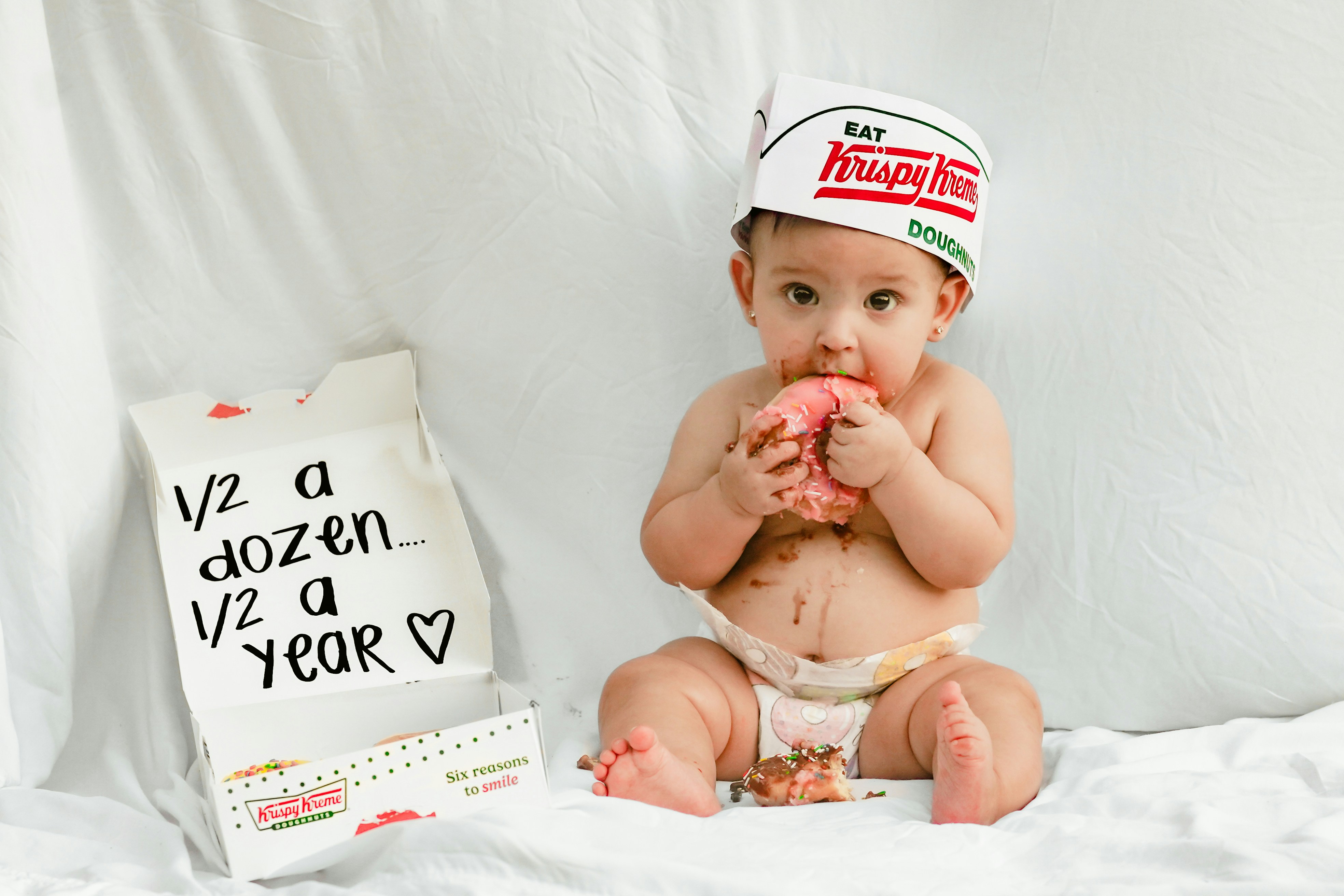 Baby eating a donut with a krispy kreme hat.