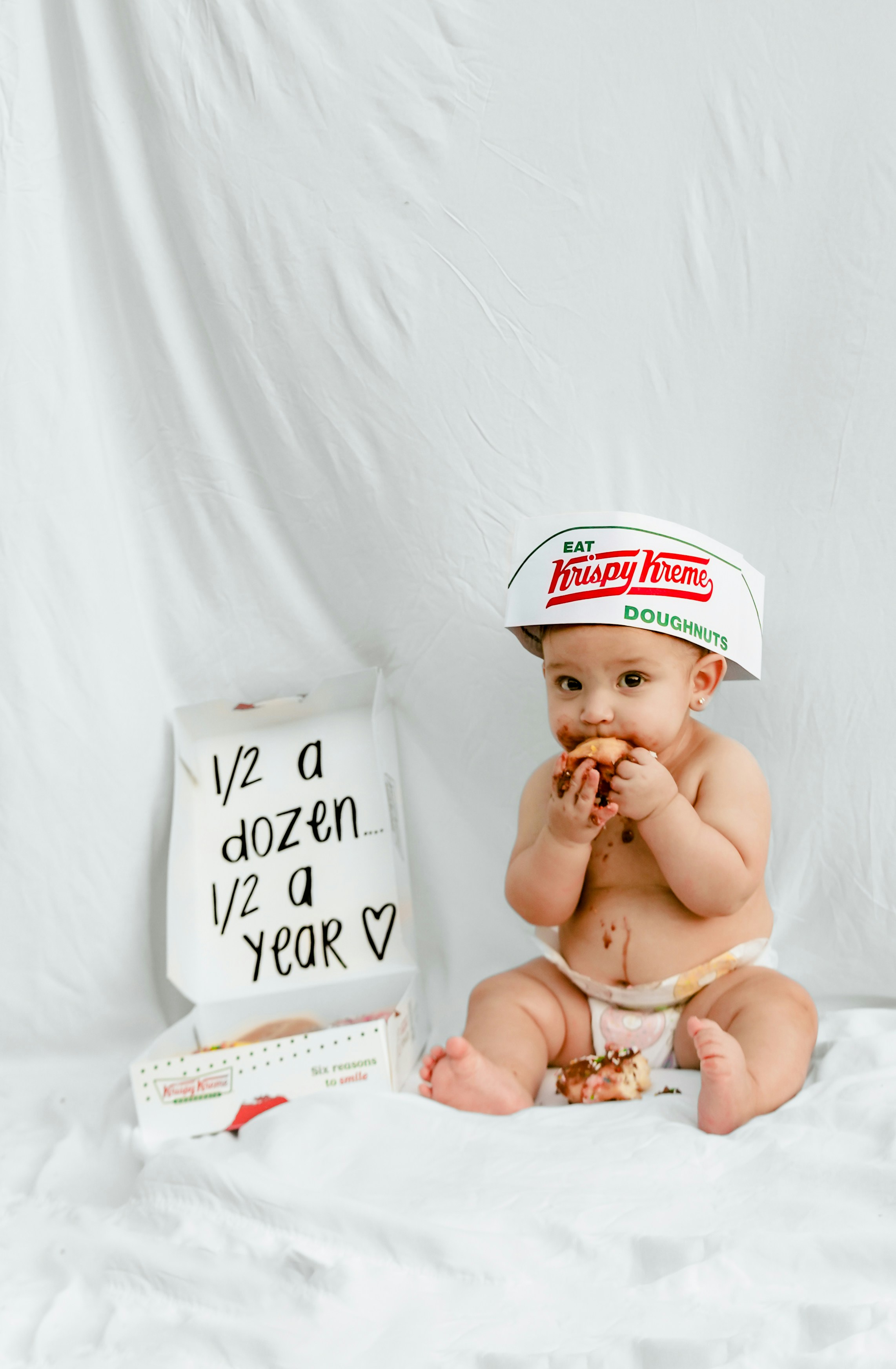 Baby eating donuts with a krispy kreme hat.