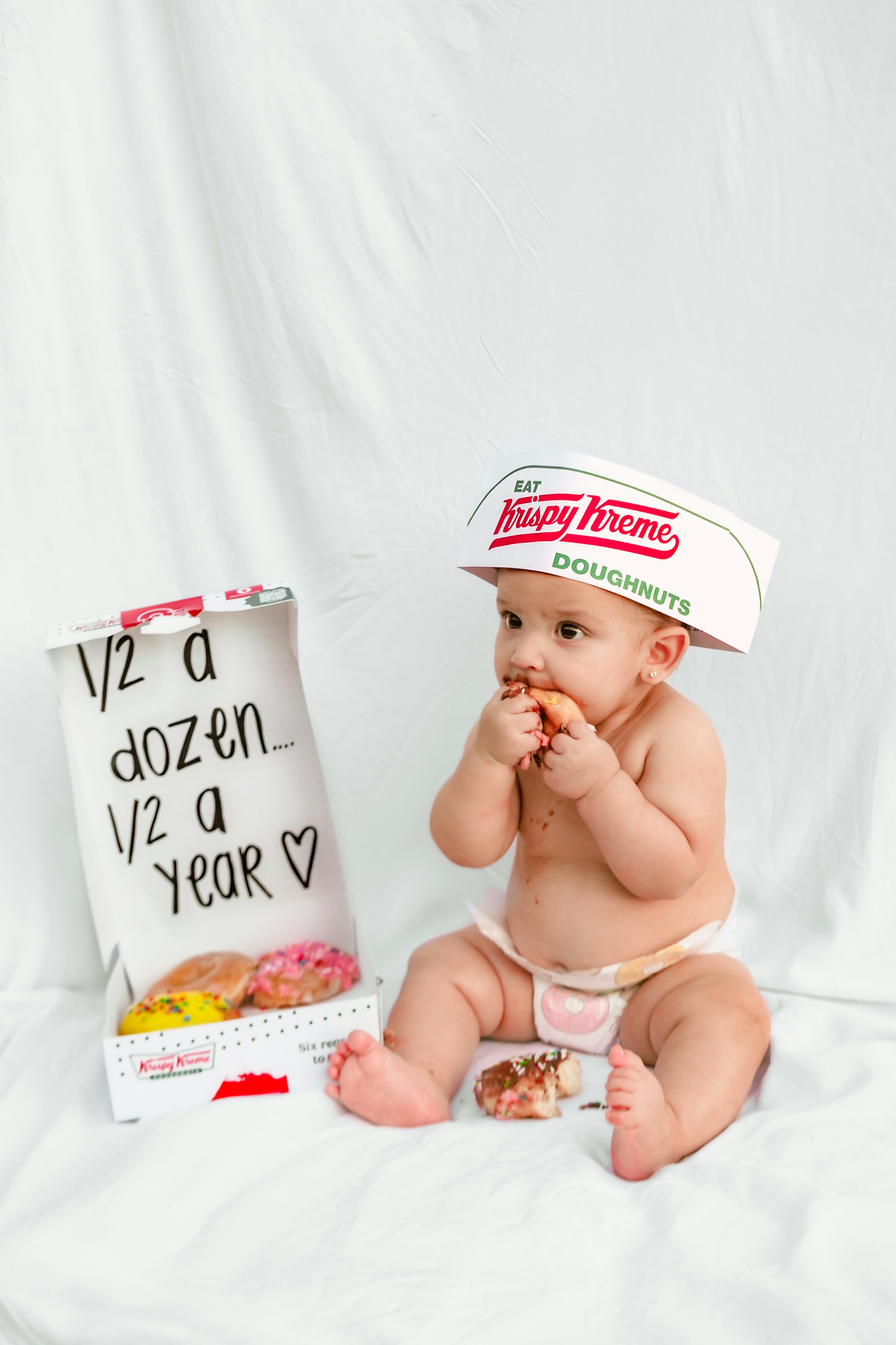 Baby in krispy kreme hat eats donut next to box