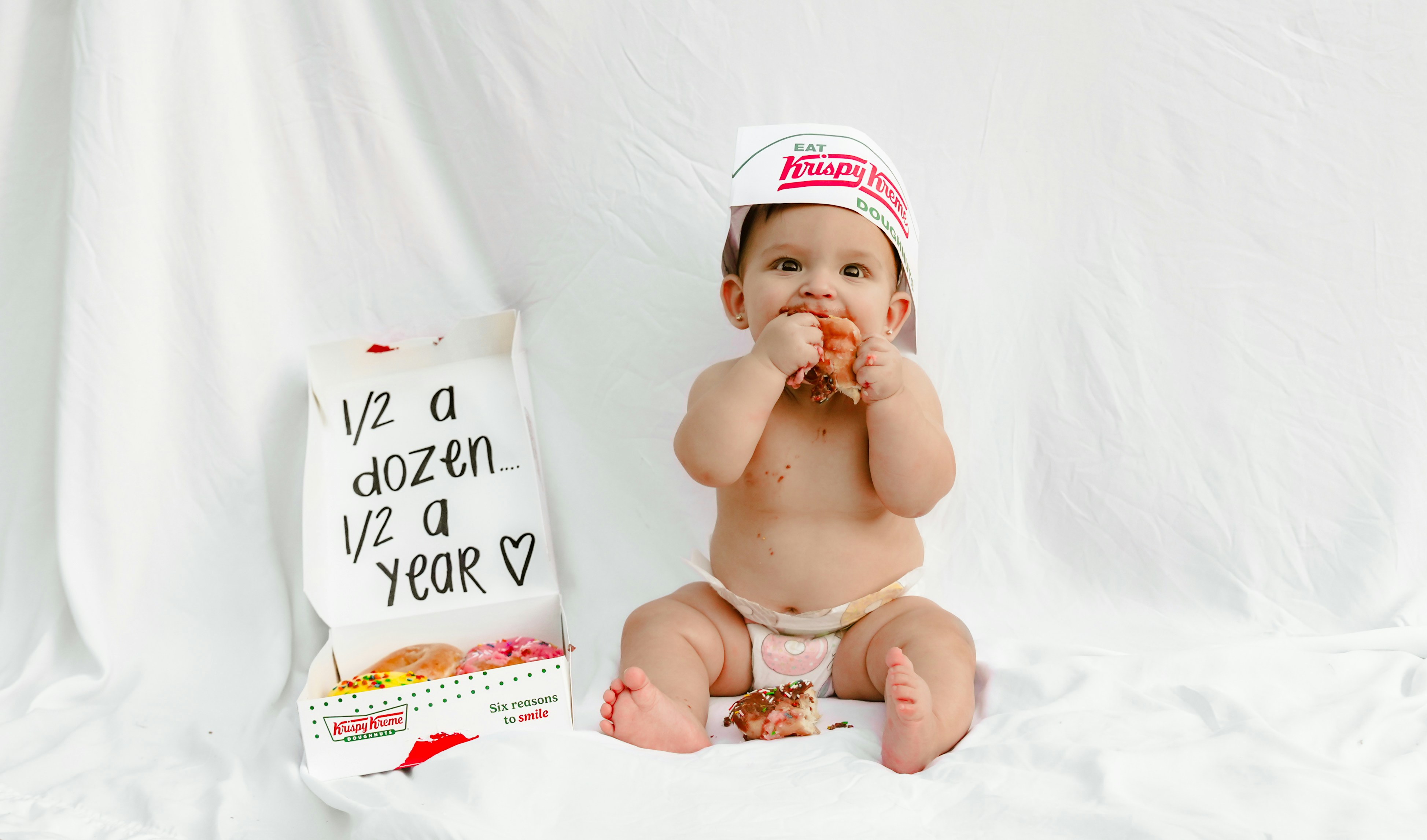 Baby eating donut with krispy kreme hat and box