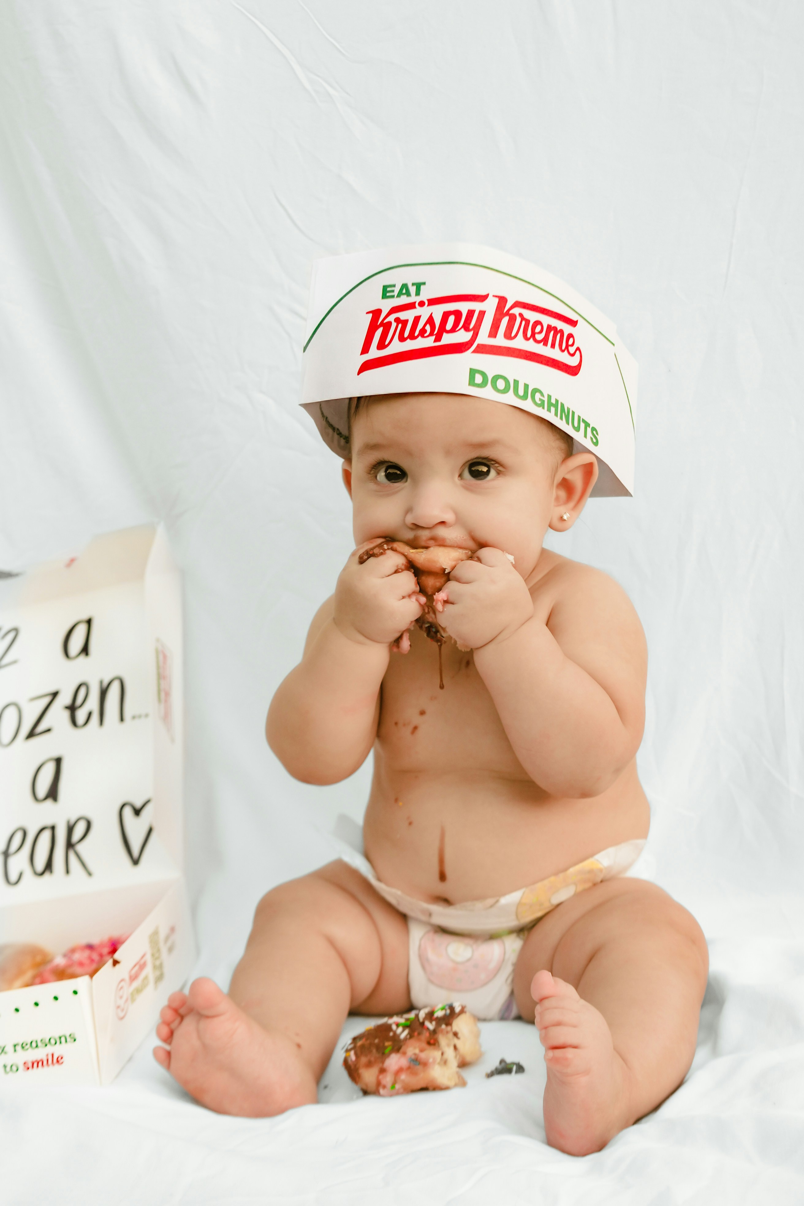 Baby wearing krispy kreme hat eats a donut