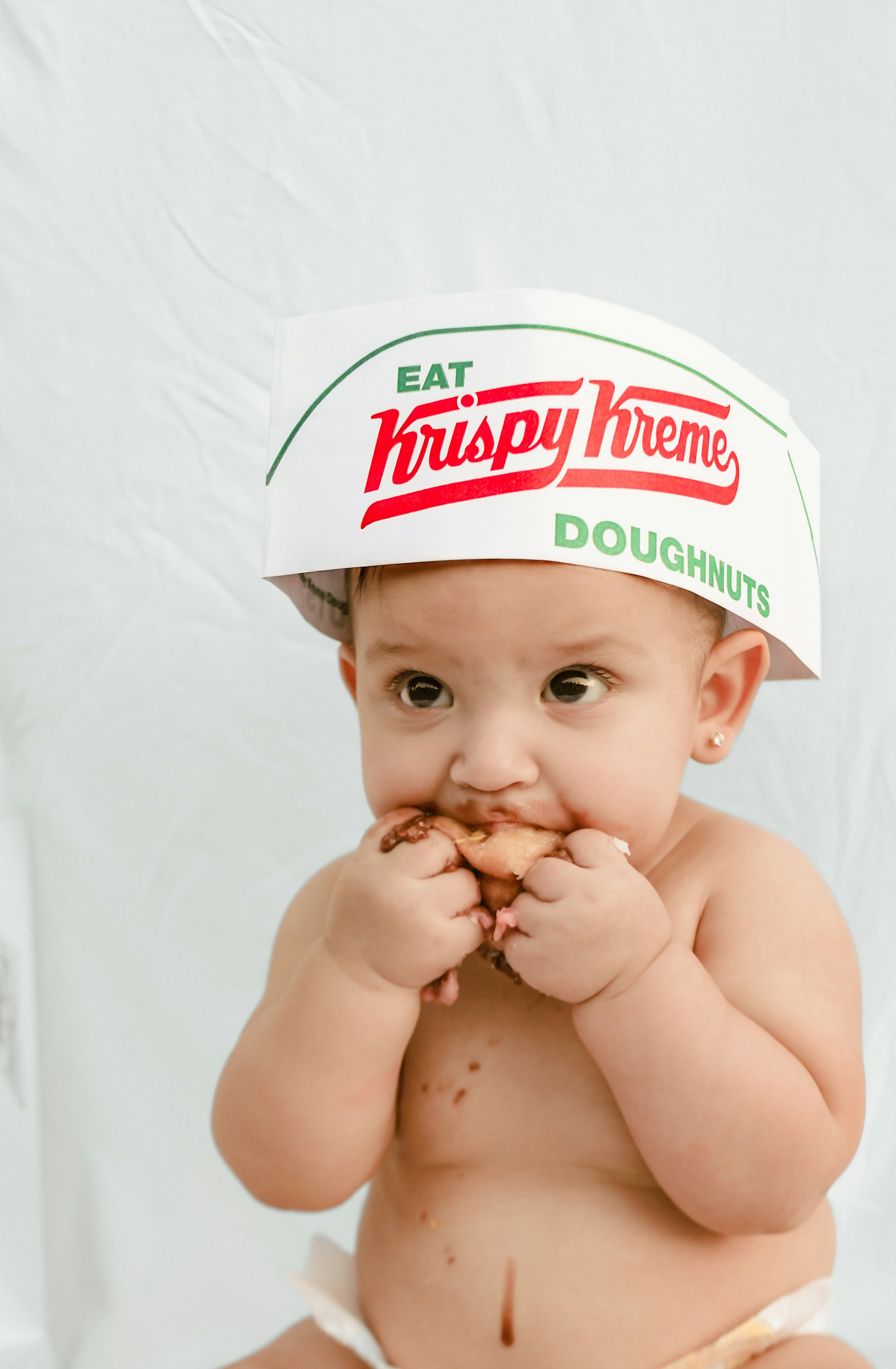 Baby wearing krispy kreme hat eating a doughnut
