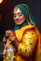 A smiling woman in a green hijab and yellow outfit.