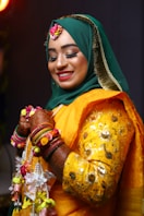 A smiling woman in a green hijab and yellow outfit.
