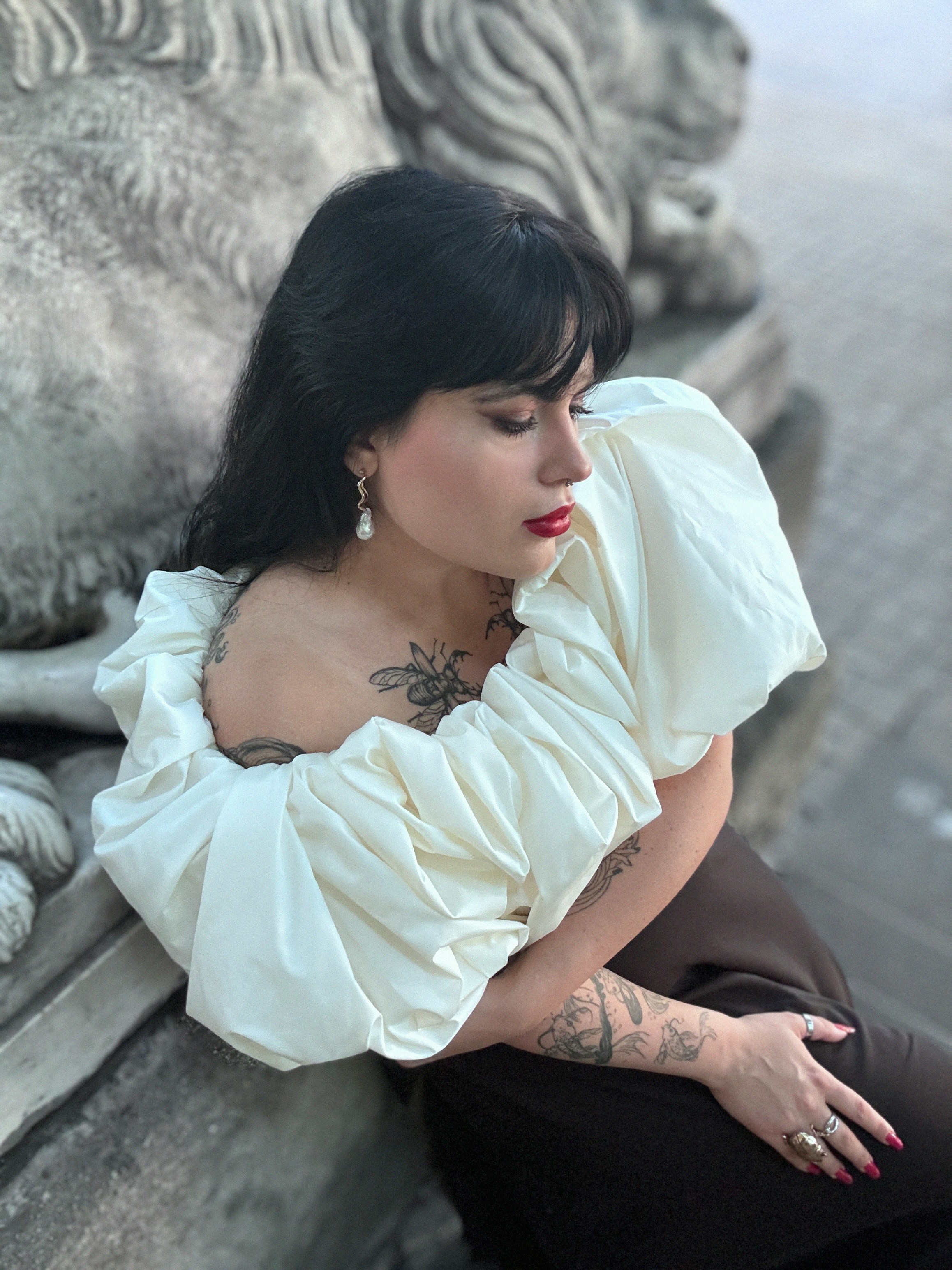 Woman in puffy sleeve top leans on stone lion.