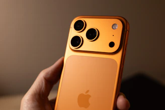 Orange smartphone with triple camera system held